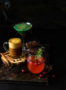 Various seasonal cocktails shot on a vintage baking sheet with smoke on a black background